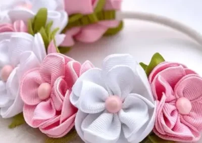 "Pink and white floral hair bow for kids, featuring fabric flowers with pink centers on a white band."