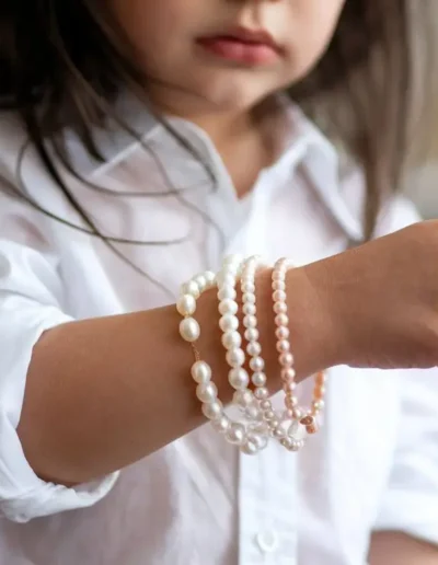 The image shows a child wearing several pearl bracelets on one arm, with a focus on the jewelry and a blurred background.