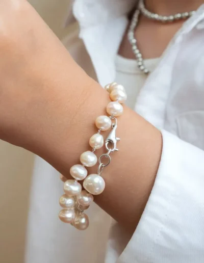 The image shows a close-up of a child’s arm wearing a simple pearl bracelet, resting on a patterned cushion