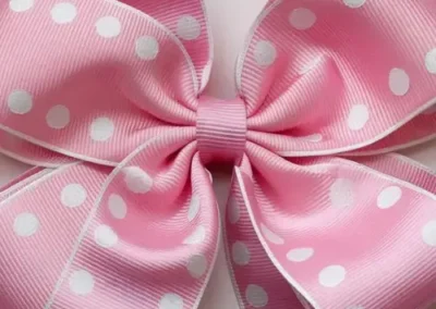 Pink polka dot hair bow with white edges and a large, neatly tied ribbon featuring white spots on a light pink background.