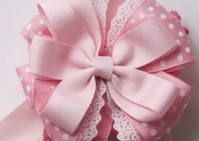 Pink layered hair bow with polka dots and lace detailing, featuring a central ribbon and long trailing ends.