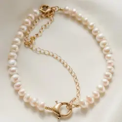  "A delicate pearl necklace featuring a gold chain and clasp, beautifully displayed on soft white fabric."