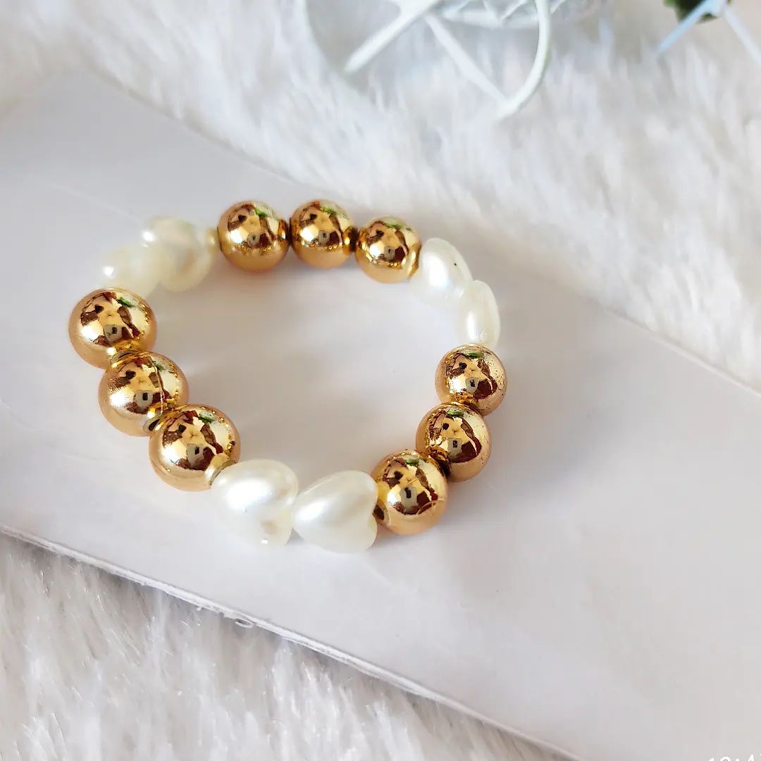  A bracelet with alternating golden round beads and white heart-shaped pearl-like beads on a white background.